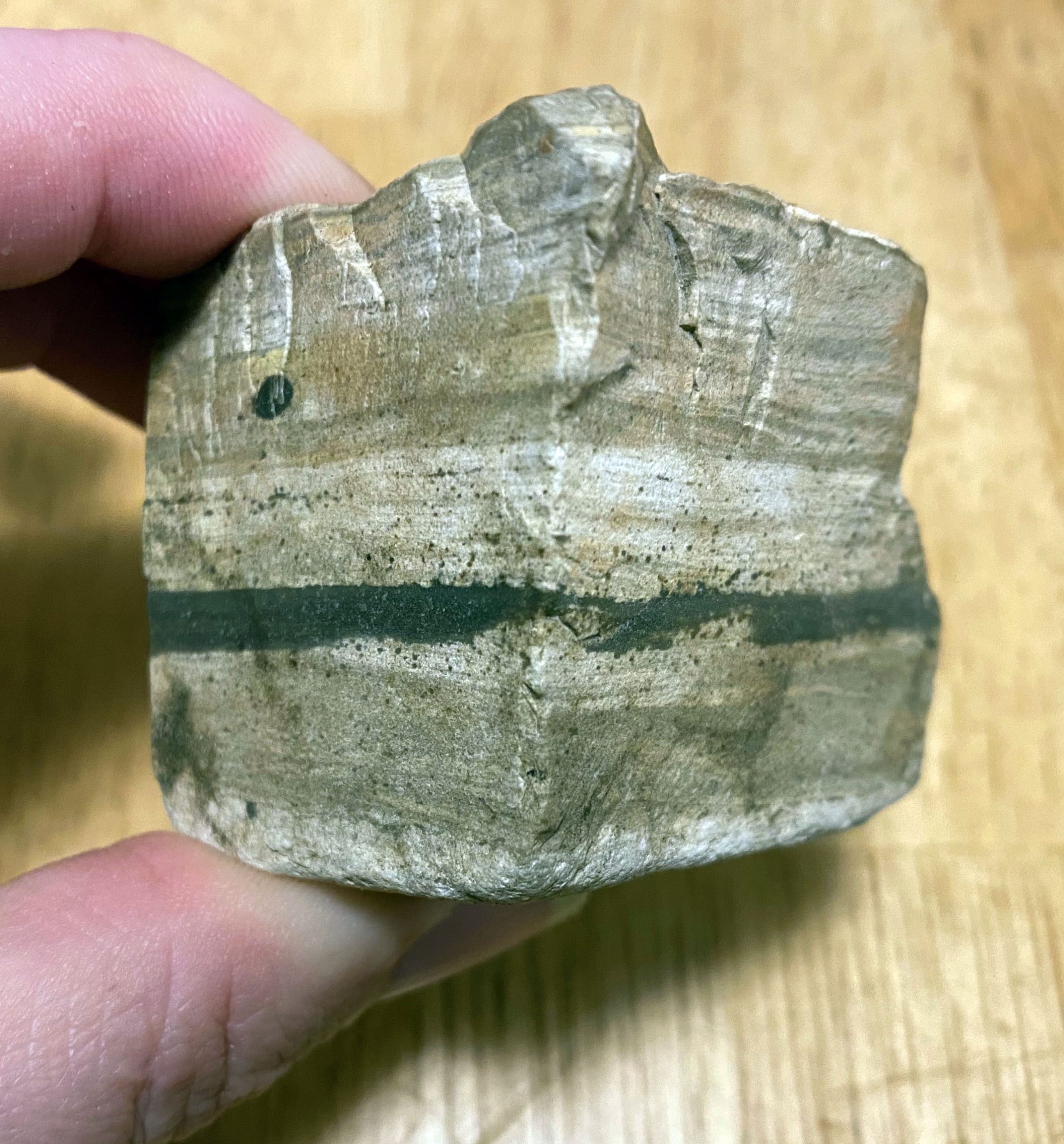 A rock irregularly cube-shaped, a couple inches on a side. White top and bottom with banding in various shades of gray and black, with one prominent black band.