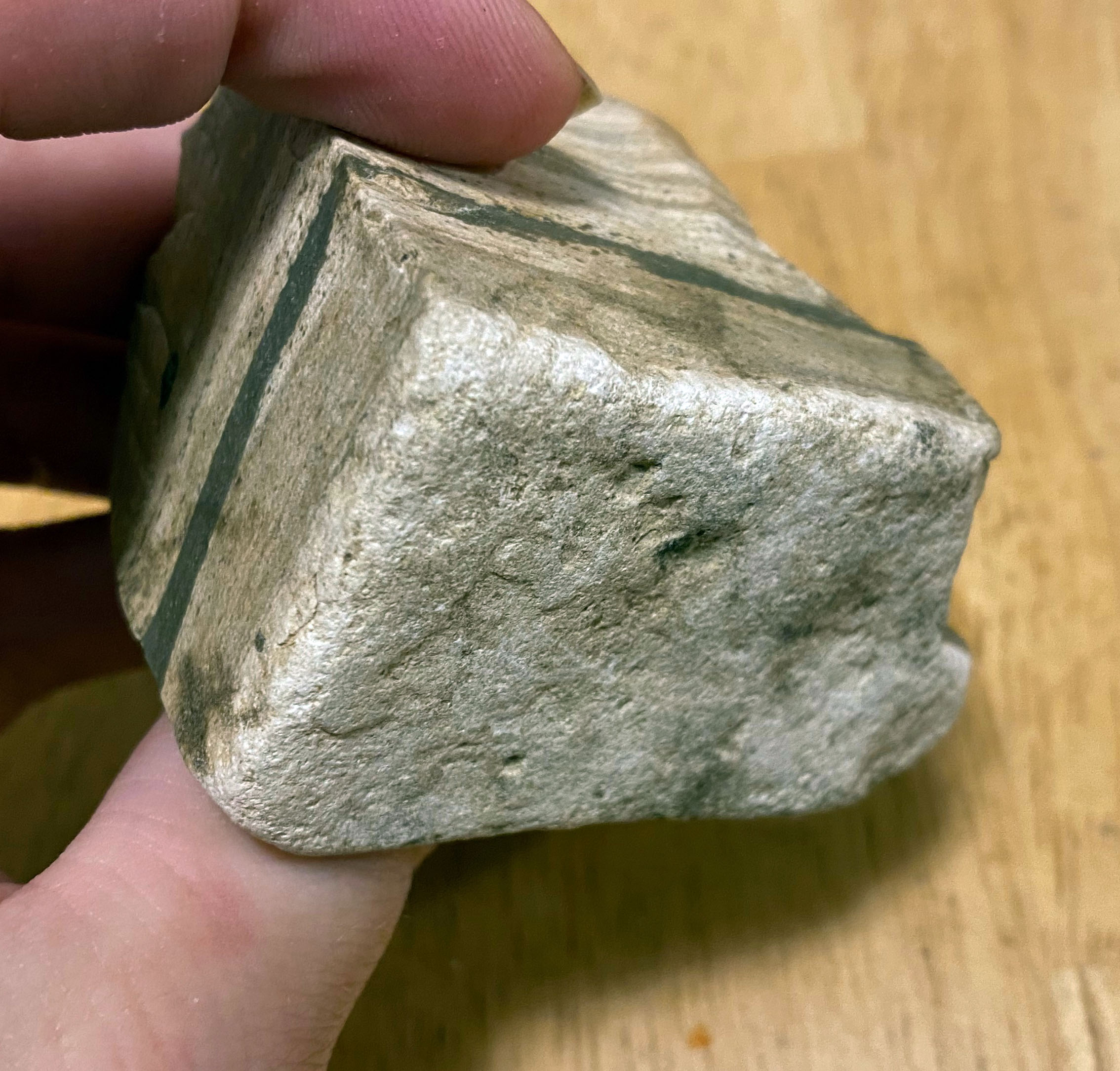 Another view of a rock irregularly cube-shaped, a couple inches on a side. White top and bottom with banding in various shades of gray and black, with one prominent black band.