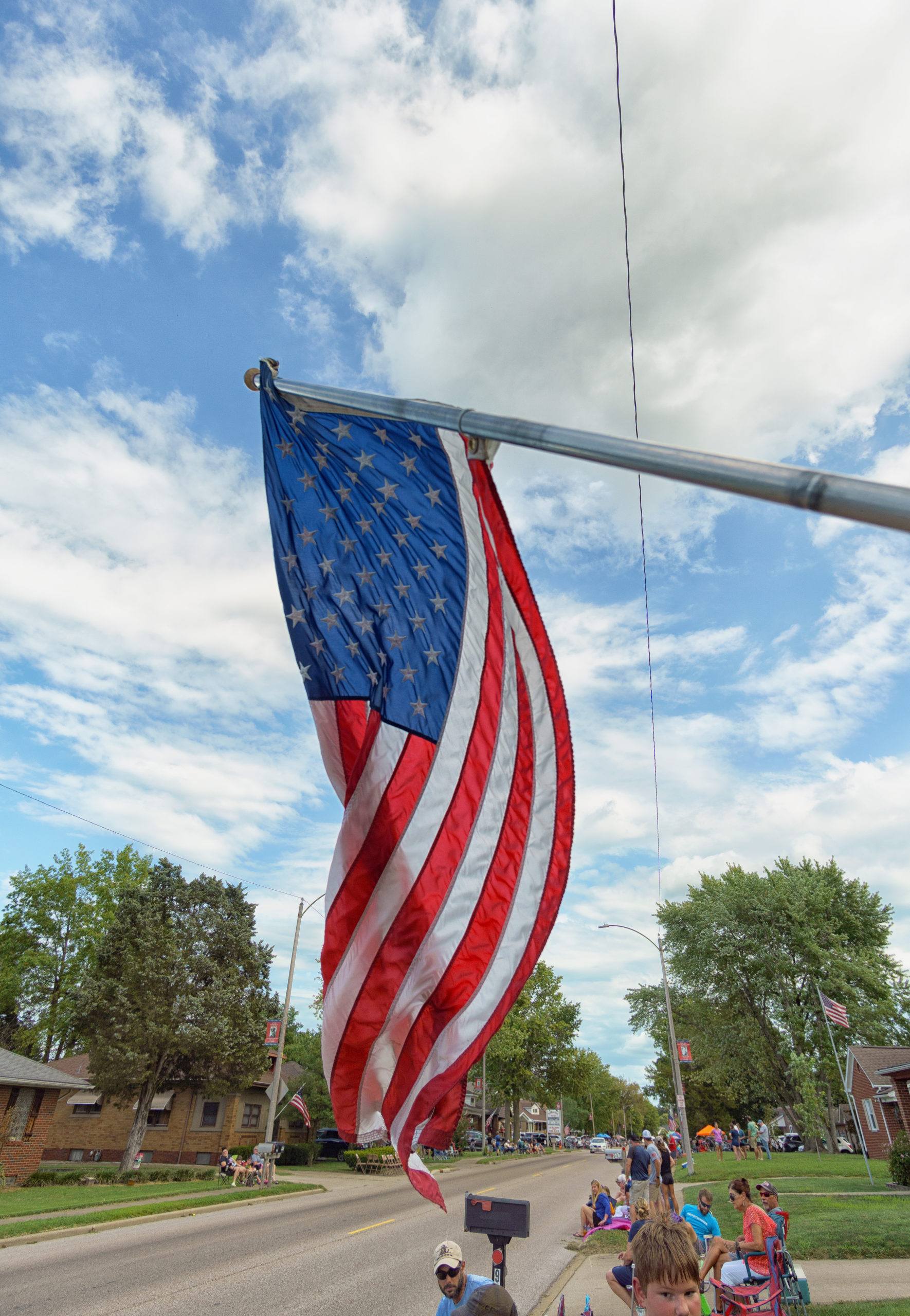 An American flag blows on a flagpole beside a small town street.